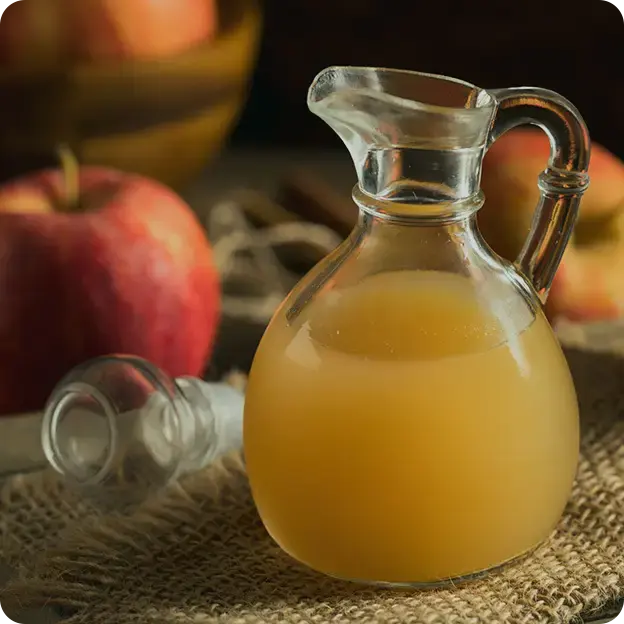 Apple cider in a pitcher with apples in the background.