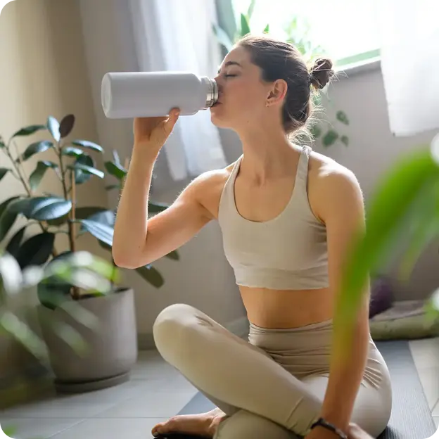 Woman drinking water on yoga mat.