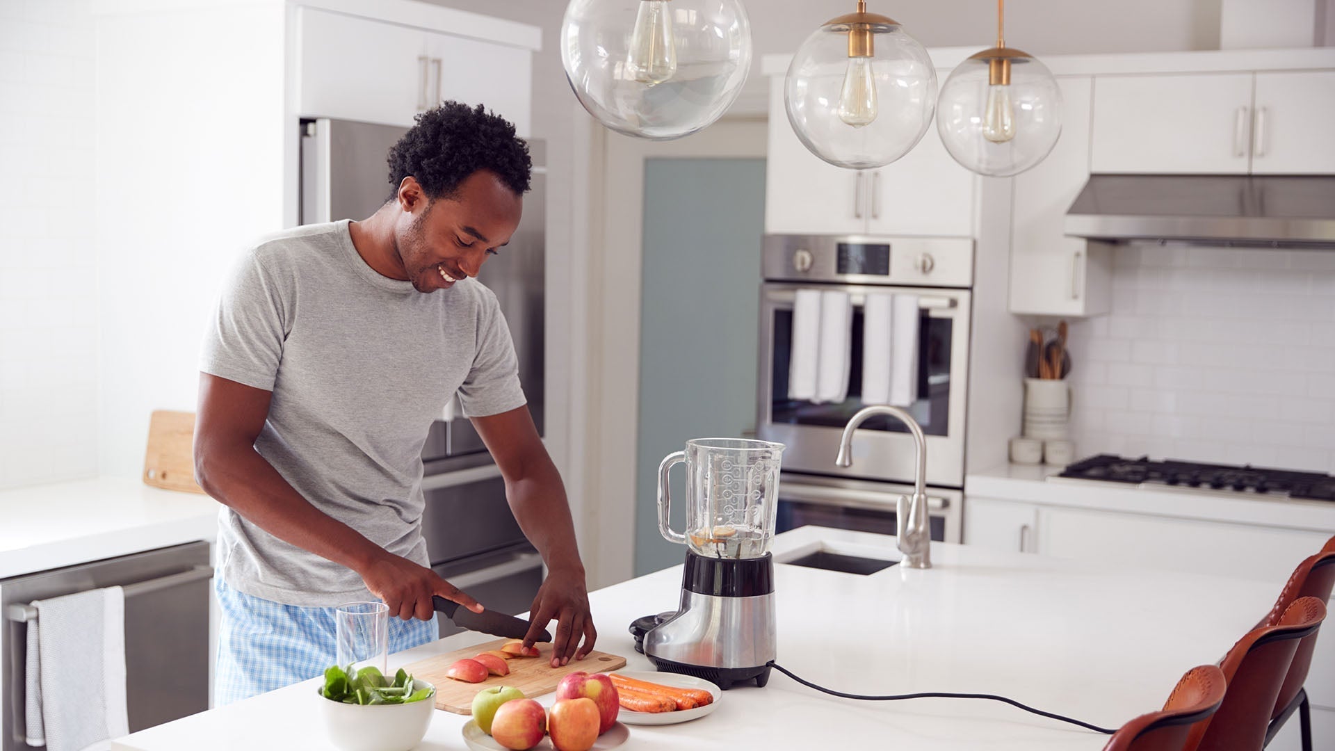 Man chopping fruit beside a blender in a bright modern kitchen.