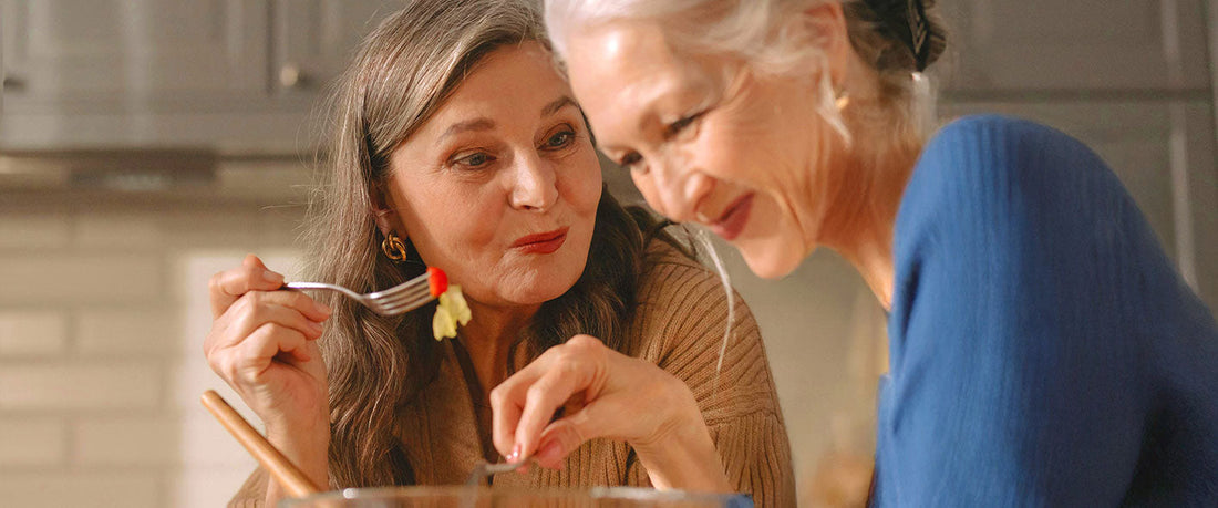 Mother and daughter eating salad in the kitche while chatting.