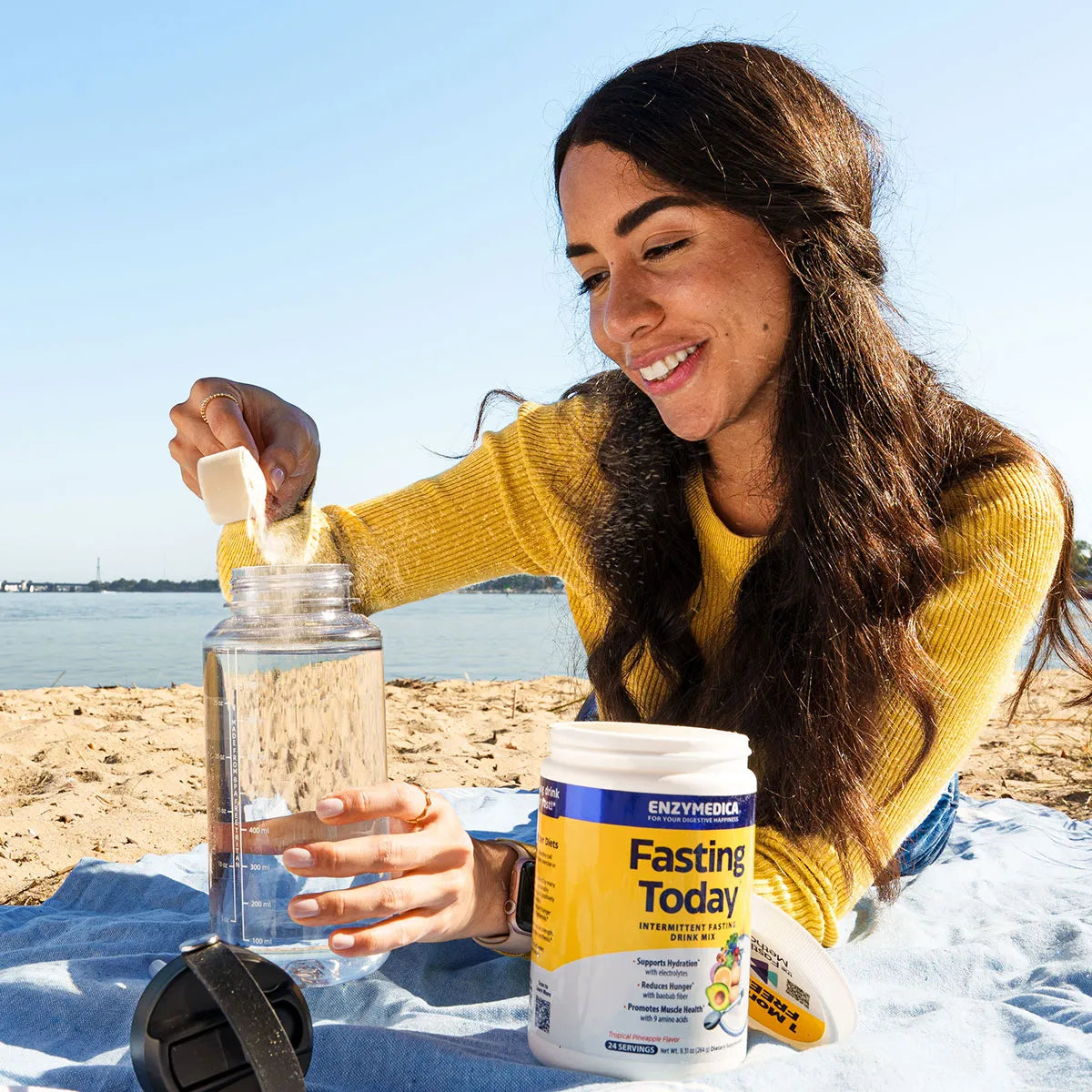Person mixing Enzymedica Fasting Today drink mix powder into a water bottle while sitting on the beach.