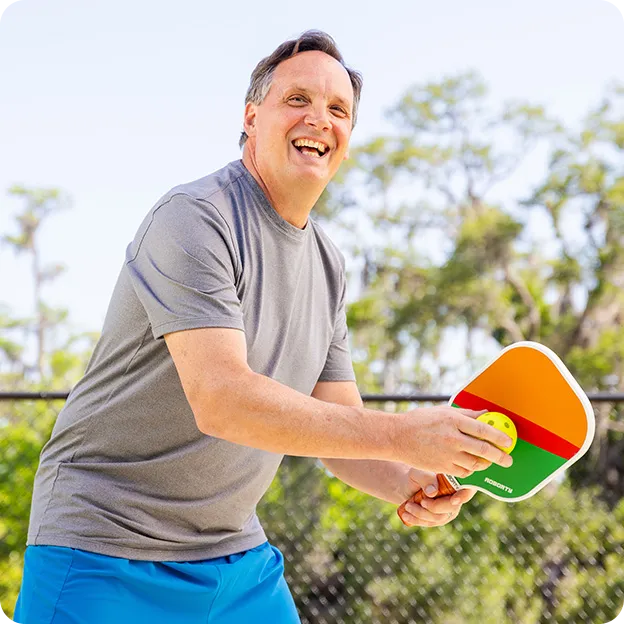 Man holding a colorful paddle outdoors with trees in the background