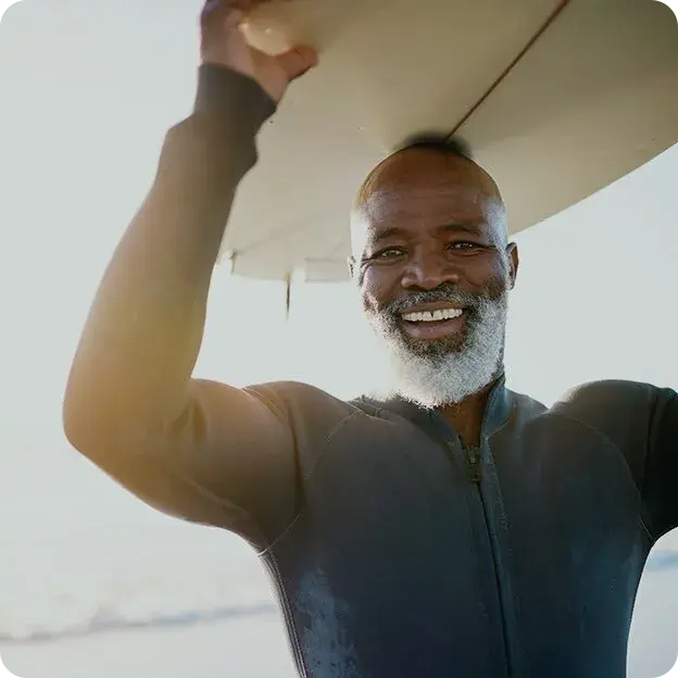 An older man smiling holding a surf board.