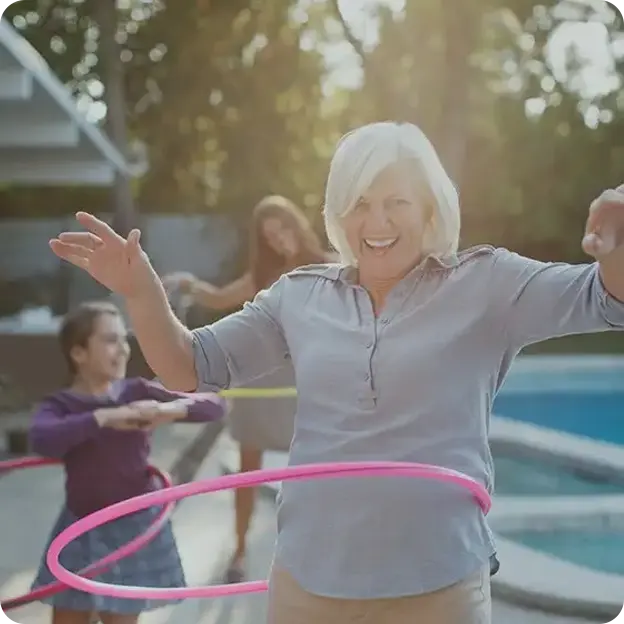 An older woman playing with a hula hoop with family.