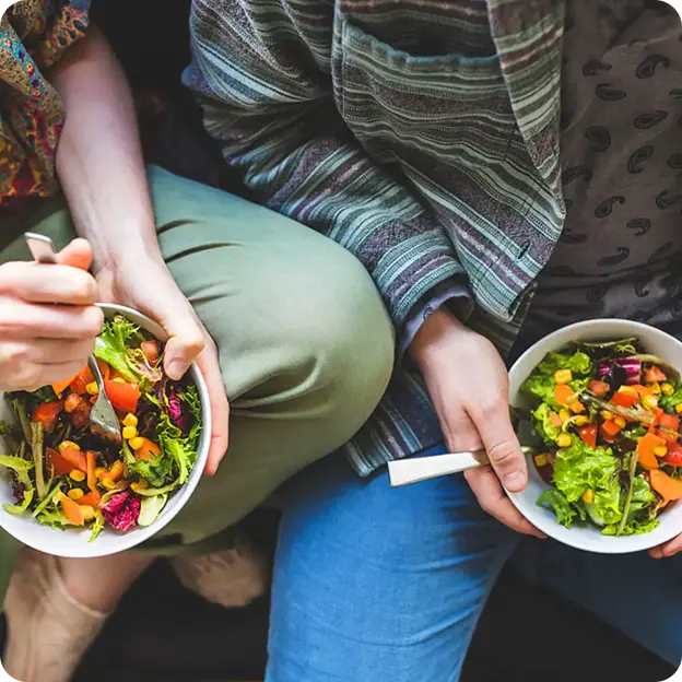Two people holding a bowl of salad.